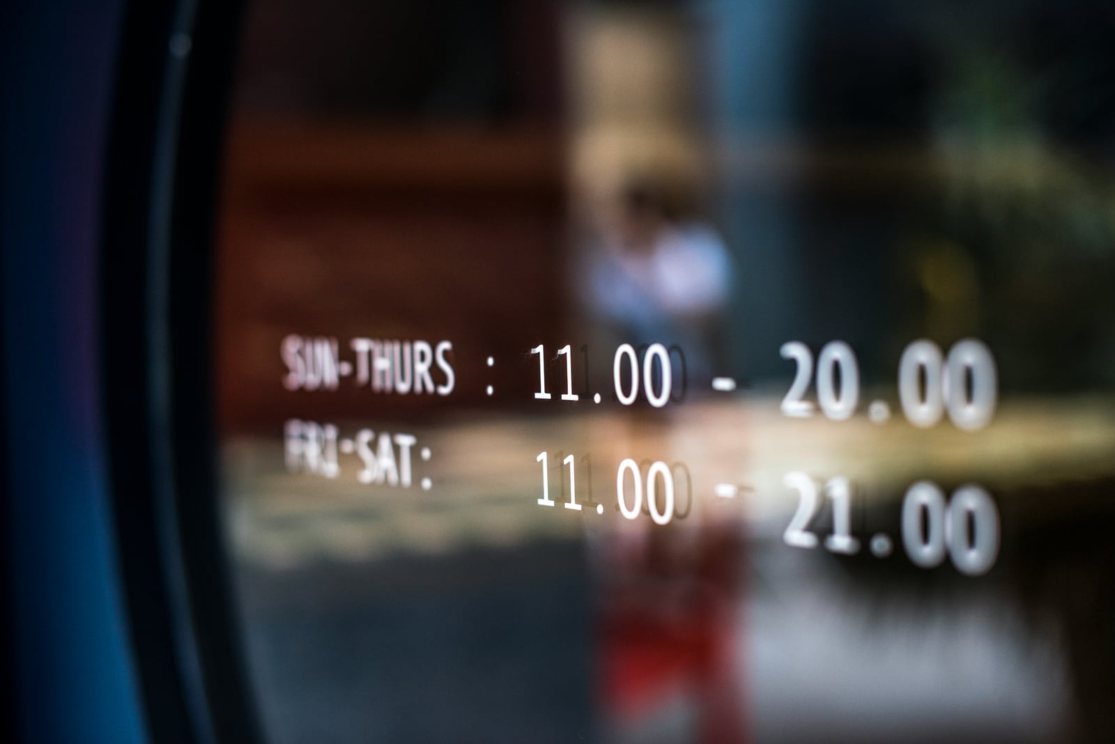 Opening hours displayed in white lettering on a glass shopfront