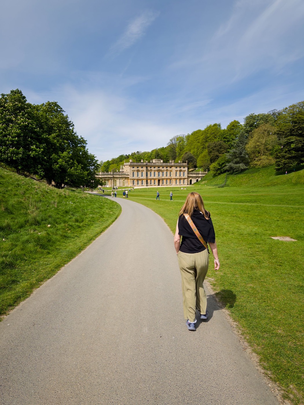 A visitor walking through green English parkland towards a historic house